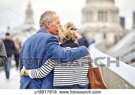 Stock Photo - Rear view of romantic mature dating couple crossing Millennium Bridge, London, UK. Fotosearch
