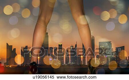 Stock Photography - Rear view of woman legs wearing high heel shoes and skyscrapers on skyline at sunset, Doha, Qatar. Fotosearch