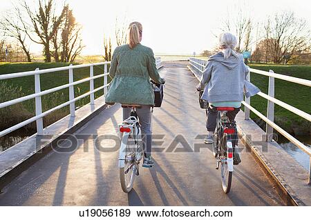 Rear view of women cycling bicycles on bridge across river View Large Photo Image Stock Photo - Rear view of women cycling bicycles on bridge across river. Fotosearch