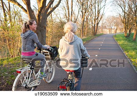 Rear view of women cycling on tree lined road View Large Photo Image Stock Photo - Rear view of women cycling on tree lined road. Fotosearch