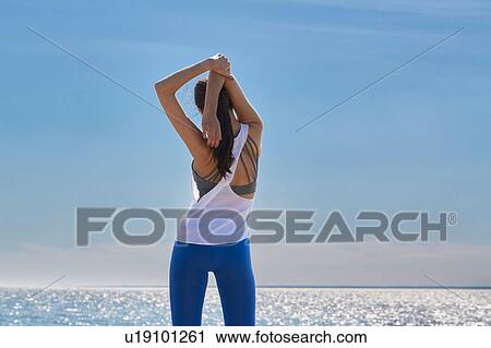 Rear view of young woman arms raised hands behind head stretching View Large Photo Image Stock Image - Rear view of young woman arms raised hands behind head stretching. Fotosearch