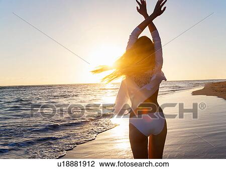 Stock Image - Rear view of young woman dancing with arms raised on beach, Dominican Republic, The Caribbean. Fotosearch