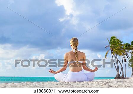 Stock Image - Rear view of young woman practising lotus pose on beach, Dominican Republic, The Caribbean. Fotosearch