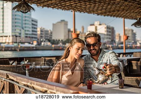 Stock Photo - Romantic couple pouring tea at Dubai marina cafe, United Arab Emirates. Fotosearch