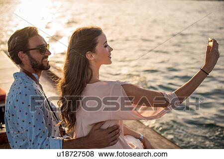Stock Photo - Romantic couple taking smartphone selfie on boat at Dubai marina, United Arab Emirates. Fotosearch