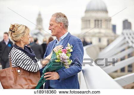 Stock Image - Romantic mature dating couple greeting each other on Millennium Bridge, London, UK. Fotosearch