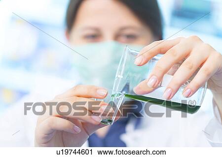 Stock Image - Scientist pouring green liquid into a cup. Fotosearch