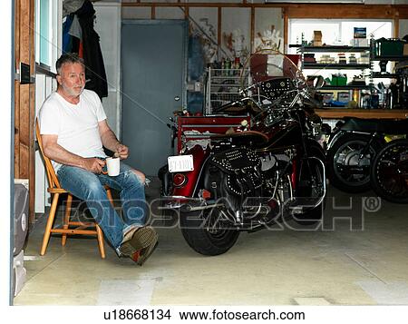Senior man sitting with a coffee in garage with motorcycle View Large Photo Image Picture - Senior man sitting with a coffee in garage with motorcycle. Fotosearch