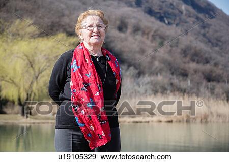 Senior woman wearing scarf in front of lake looking at camera smiling View Large Photo Image Stock Photo - Senior woman wearing scarf in front of lake looking at camera smiling. Fotosearch