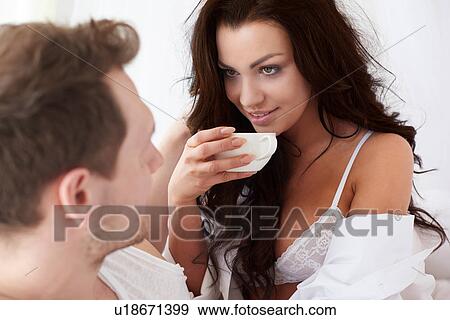 Stock Photo - Sexy young woman drinking coffee in bed with boyfriend. Fotosearch