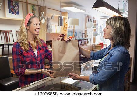 Stock Photo - Shop assistant handing shopper shopping bag. Fotosearch