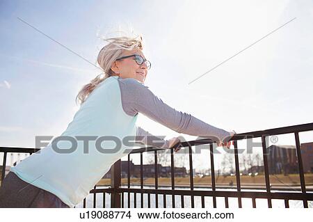 Picture - Side view of woman leaning against railing looking away. Fotosearch