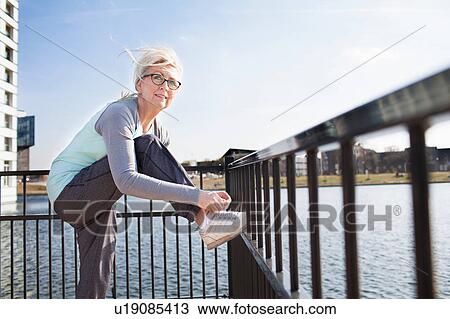 Stock Image - Side view of woman leg raised on railing tying shoelace. Fotosearch