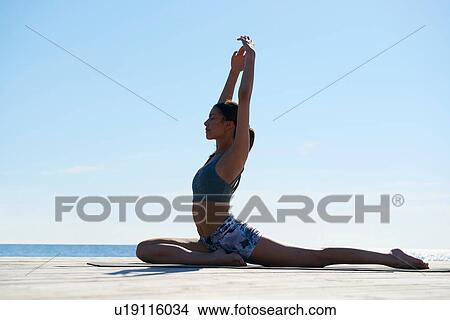 Picture - Side view of woman on pier, arms raised in yoga position. Fotosearch