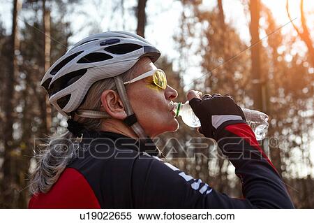 Side view of woman wearing cycling helmet and sunglasses drinking water from plastic bottle View Large Photo Image Stock Photography - Side view of woman wearing cycling helmet and sunglasses drinking water from plastic bottle. Fotosearch