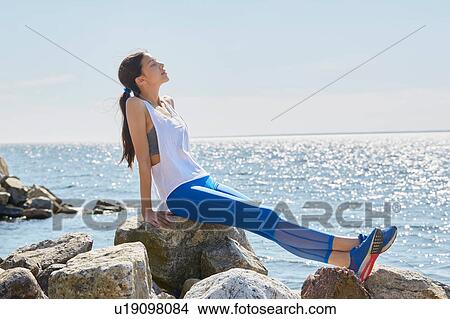 Side view of woman wearing sports clothes sitting on rocks basking in sunlight View Large Photo Image Picture - Side view of woman wearing sports clothes sitting on rocks basking in sunlight. Fotosearch