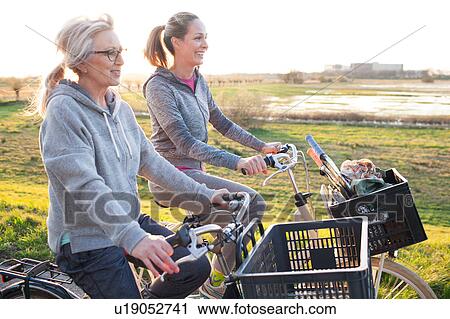 Stock Image - Side view of women cycling by marshland smiling. Fotosearch