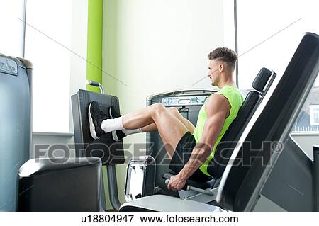 Stock Photo - Side view of young man in gym using exercise equipment. Fotosearch