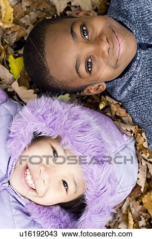 Stock Image - Smiling children lying on autumn leaves. Fotosearch