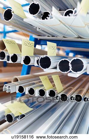 Stock Photograph - Stacked shelves of metal rods and adhesive notes in roller blind factory. Fotosearch