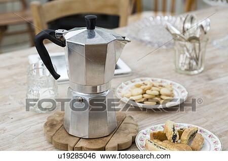 Stock Photograph - Stove top coffee pot with plates of baked good on dining table. Fotosearch