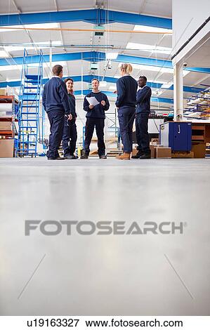Stock Photo - Surface level view of manager explaining to team in manufacturing factory. Fotosearch