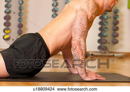 Tattooed man exercising on yoga mat in gym View Large Photo Image Picture - Tattooed man exercising on yoga mat in gym. Fotosearch
