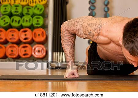 Tattooed man exercising on yoga mat in gym View Large Photo Image Stock Image - Tattooed man exercising on yoga mat in gym. Fotosearch