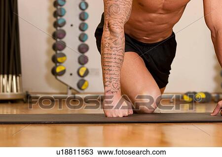 Tattooed man exercising on yoga mat in gym View Large Photo Image Stock Image - Tattooed man exercising on yoga mat in gym. Fotosearch