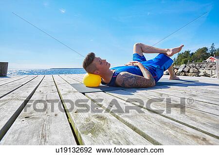 Tattooed man lying on pier using ball as pillow View Large Photo Image Stock Image - Tattooed man lying on pier using ball as pillow. Fotosearch