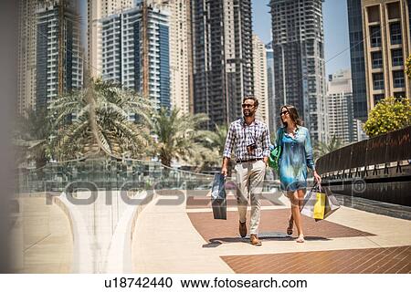 Tourist couple strolling on walkway carrying shopping bags, Dubai, United Arab Emirates View Large Photo Image Stock Image - Tourist couple strolling on walkway carrying shopping bags, Dubai, United Arab Emirates. Fotosearch