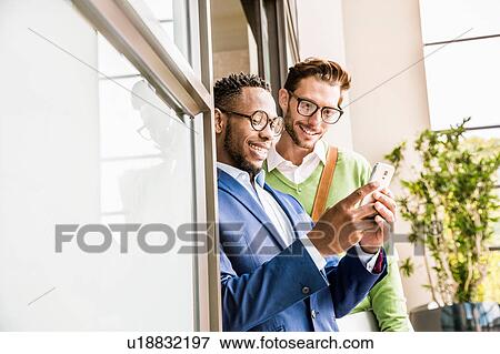 Stock Photo - Two businessmen in office doorway reading smartphone texts. Fotosearch