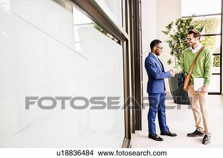 Two businessmen shaking hands outside office building View Large Photo Image Picture - Two businessmen shaking hands outside office building. Fotosearch