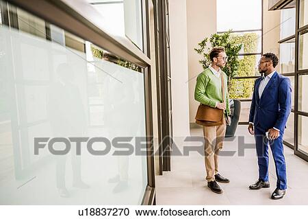 Two businessmen standing having discussion outside office building View Large Photo Image Stock Image - Two businessmen standing having discussion outside office building. Fotosearch