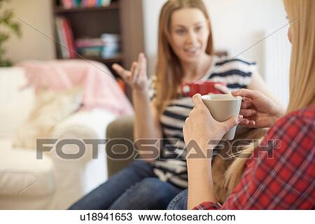 Stock Image - Two female friends, sitting on sofa, drinking coffee, catching up. Fotosearch