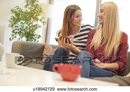 Two female friends, sitting on sofa, looking at smartphone View Large Photo Image Stock Photo - Two female friends, sitting on sofa, looking at smartphone. Fotosearch