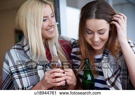 Stock Image - Two female friends, sitting outdoors, drinking bottled beer. Fotosearch