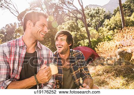 Stock Image - Two male campers chatting over coffee in forest, Deer Park, Cape Town, South Africa. Fotosearch