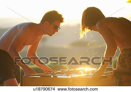 Picture - Two male friends playing table football, outdoors. Fotosearch