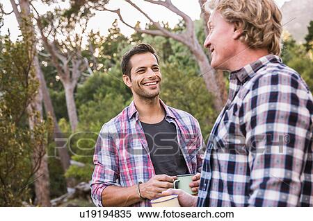 Stock Photography - Two male hikers chatting over coffee in forest, Deer Park, Cape Town, South Africa. Fotosearch