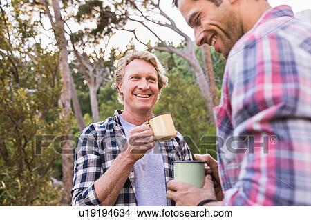 Picture - Two male hikers talking over coffee in forest, Deer Park, Cape Town, South Africa. Fotosearch