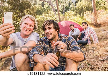 Stock Image - Two men taking smartphone selfie camping in forest, Deer Park, Cape Town, South Africa. Fotosearch