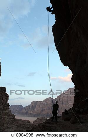 Stock Photo - Two silhouetted people rappelling down rock face, Wadi Rum, Jordan. Fotosearch