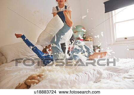 Picture - Two sister having feather pillow fight on bed. Fotosearch