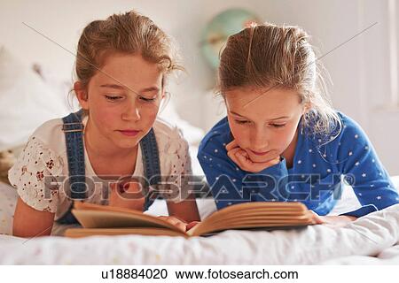 Two sisters lying on bed reading a book View Large Photo Image Stock Image - Two sisters lying on bed reading a book. Fotosearch