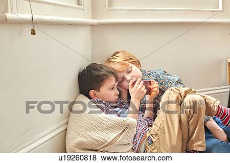 Two young boys leaning, sitting indoors, against wall, looking at smartphone View Large Photo Image Stock Photo - Two young boys leaning, sitting indoors, against wall, looking at smartphone. Fotosearch
