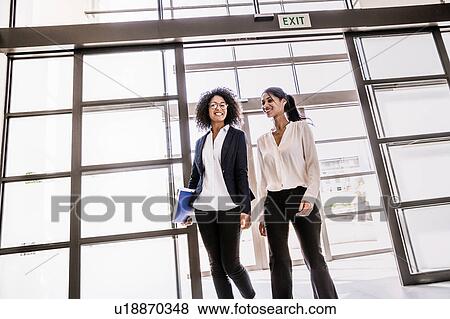 Two young businesswomen arriving at office entrance View Large Photo Image Stock Photo - Two young businesswomen arriving at office entrance. Fotosearch