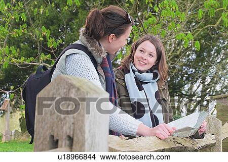 Two young women in rural landscape, leaning on wooden fence, holding map View Large Photo Image Picture - Two young women in rural landscape, leaning on wooden fence, holding map. Fotosearch