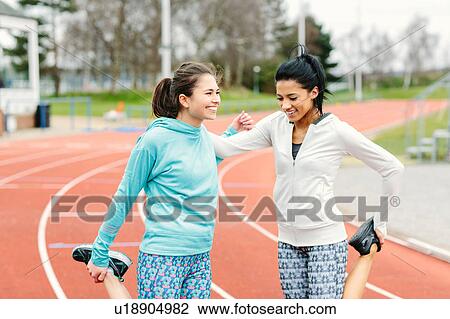 Stock Image - Two young women on running track, exercising, stretching. Fotosearch