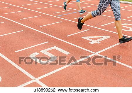 Stock Image - Two young women running on running track, low section. Fotosearch